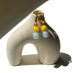 Pair of mango jade and aquamarine charms on gold hoops, hung on a ceramic arch vase in sunlight