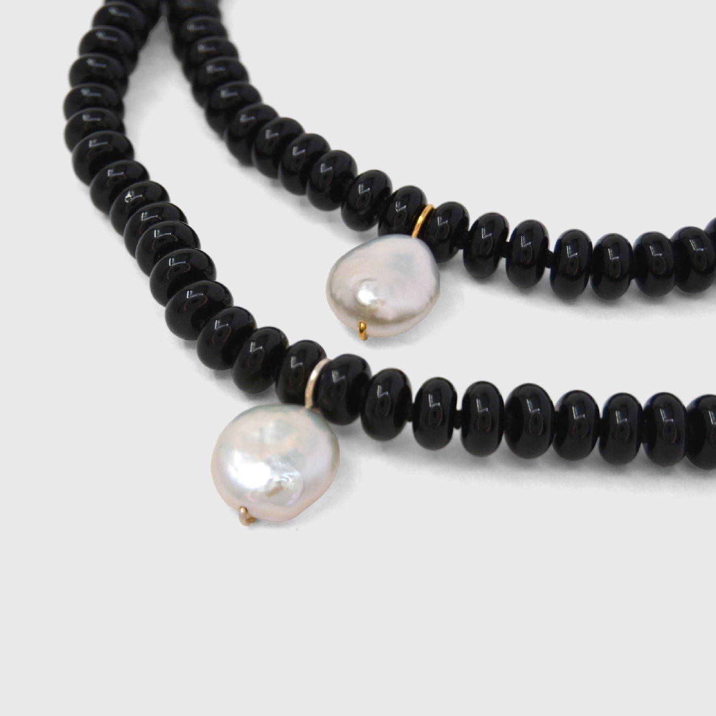 Black beaded necklace with white pearls on a light grey background