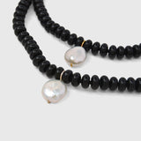 Black beaded necklace with white pearls on a light grey background