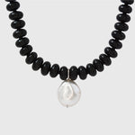 Necklace with black beads and a white pearl on a light grey background