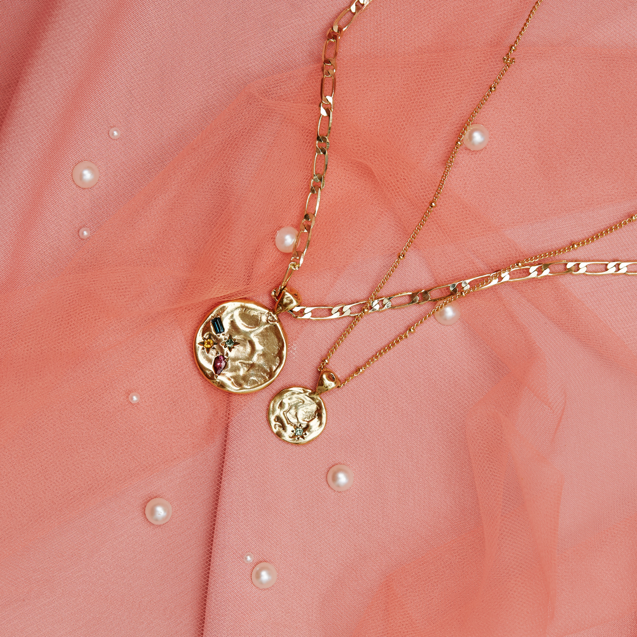 Gold necklaces with round pendants on a pink fabric background