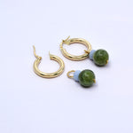 Two angelite and Canada jade charms, one hung on a gold hoop earring and one lying beside an open hoop