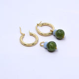 Two angelite and Canada jade charms, one hung on a gold hoop earring and one lying beside an open hoop