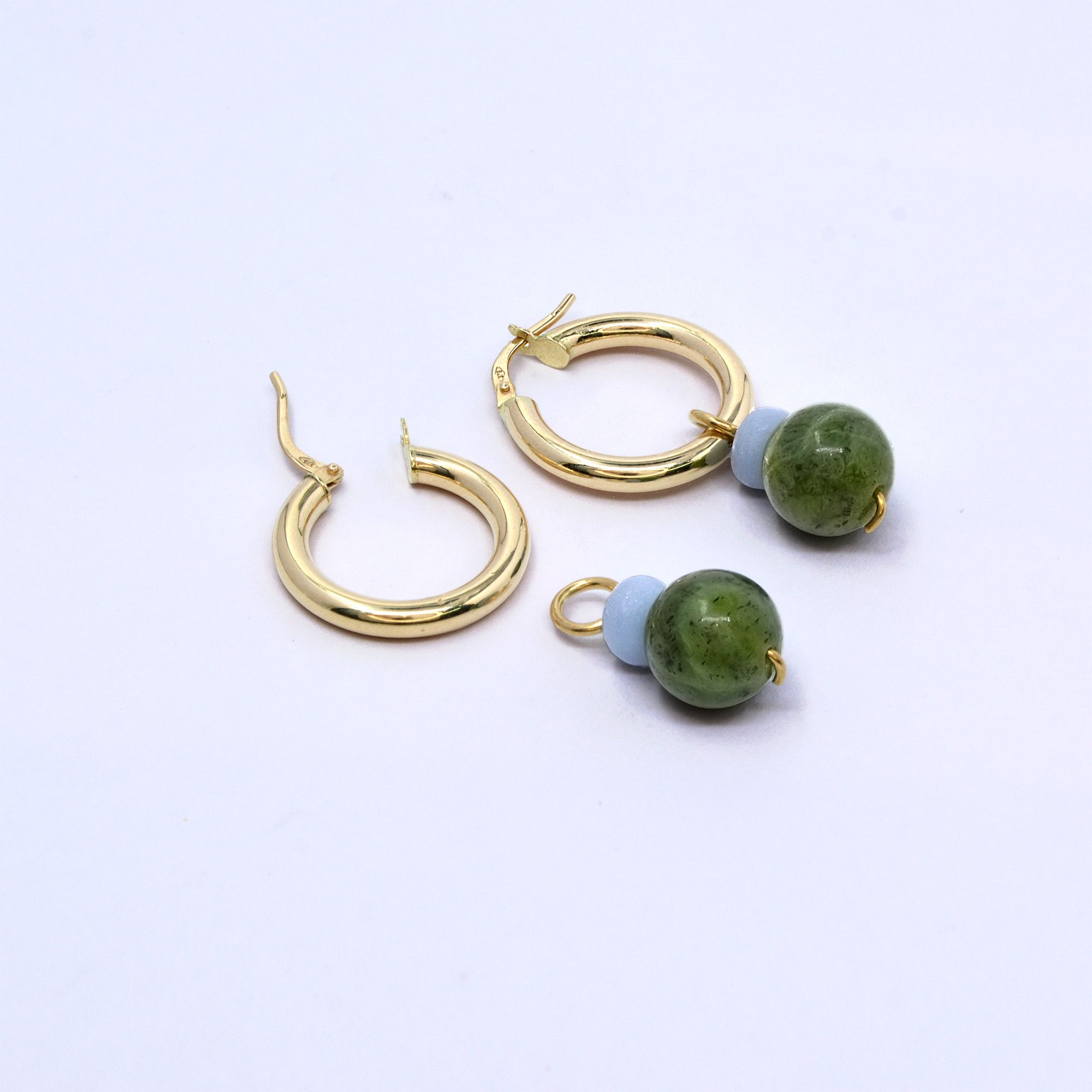 Two angelite and Canada jade charms, one hung on a gold hoop earring and one lying beside an open hoop